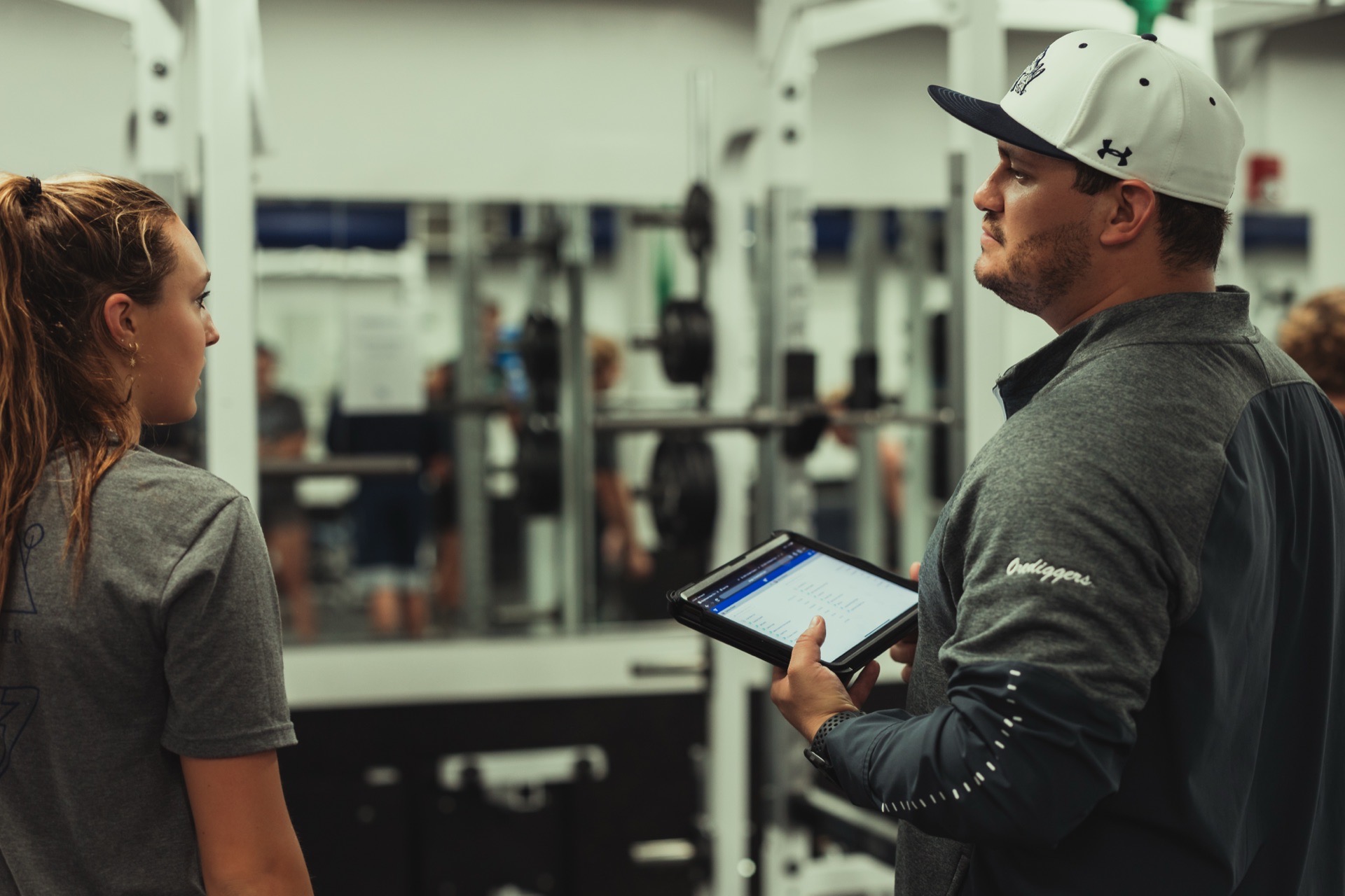 A coach with a tablet supervising athletes in a school weight room